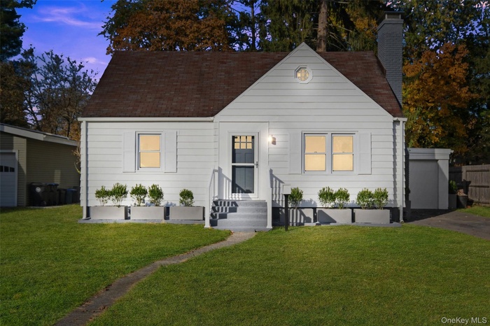 View of front of home featuring a front yard, a chimney, and a shingled roof
