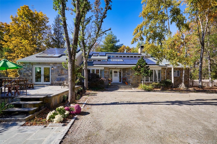 Mid-century modern home with stone siding, french doors, roof mounted solar panels, and a wooden deck