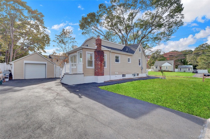 View of front facade featuring a detached garage, an outdoor structure, driveway, a chimney, and a front yard