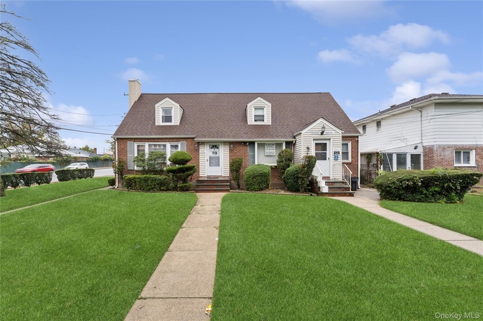 Cape cod house with brick siding, a front lawn, roof with shingles, and a chimney
