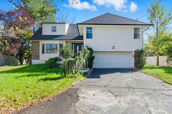 Split level home with a shingled roof, an attached garage, asphalt driveway, and stucco siding