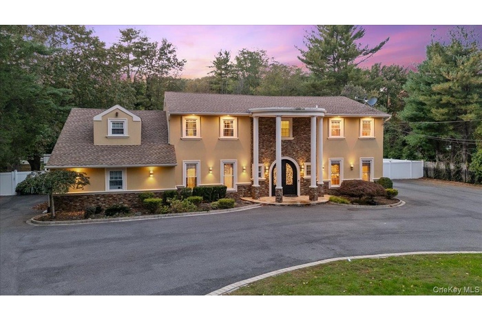 Greek revival inspired property featuring stone siding, stucco siding, driveway, and roof with shingles