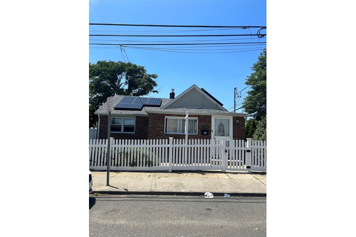 View of front of home with brick siding, solar panels, a fenced front yard, and a chimney