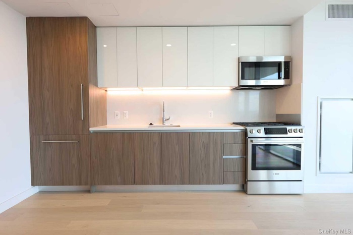 Kitchen featuring modern cabinets, stainless steel appliances, white cabinets, and brown cabinets