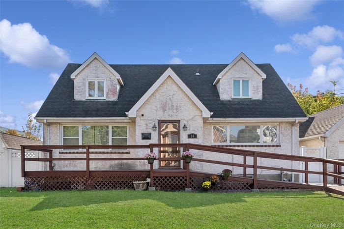 New england style home featuring roof with shingles, a deck, and a front lawn