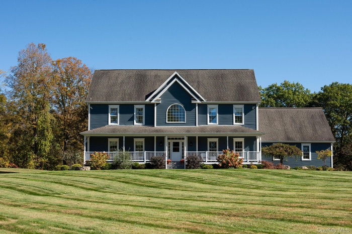 Colonial house featuring a porch, a front lawn, and roof with shingles