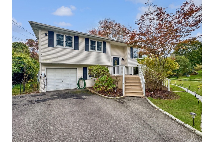 Raised ranch with an attached garage, asphalt driveway, a front lawn, and stairs