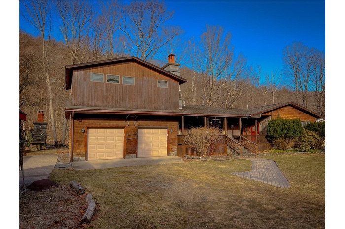View of front of property featuring a chimney, a front lawn, driveway, a porch, and a garage