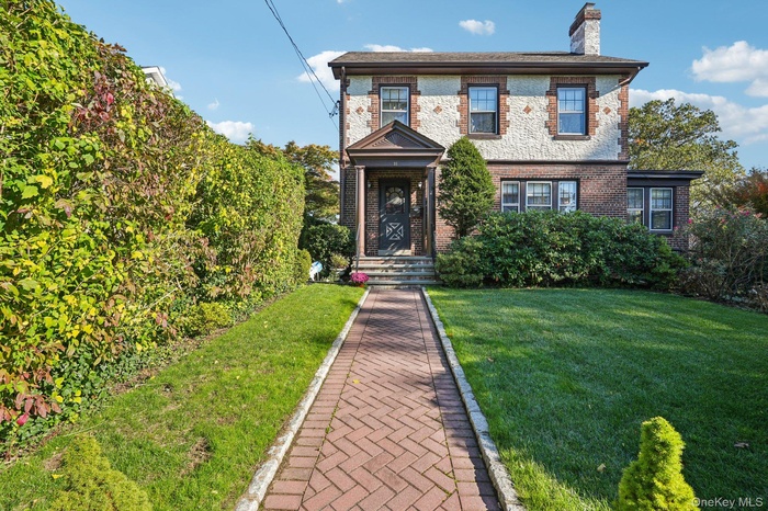 View of front facade with brick siding, a chimney, and a front yard
