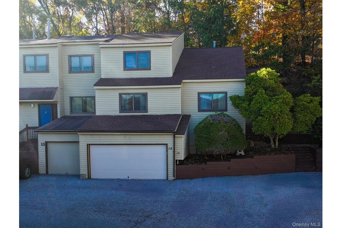 Traditional-style home featuring an attached garage, roof with shingles, driveway, and view of wooded area