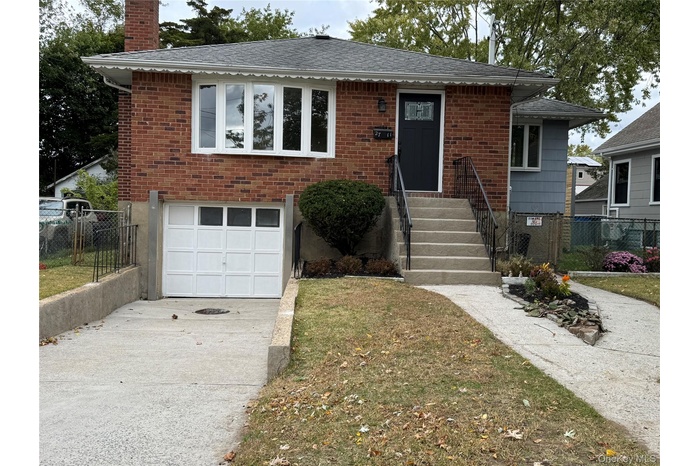 View of front of home with concrete driveway, a garage, a chimney, and brick siding
