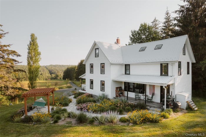 Rear view of house featuring a chimney, a metal roof, a pergola, a yard, and covered porch