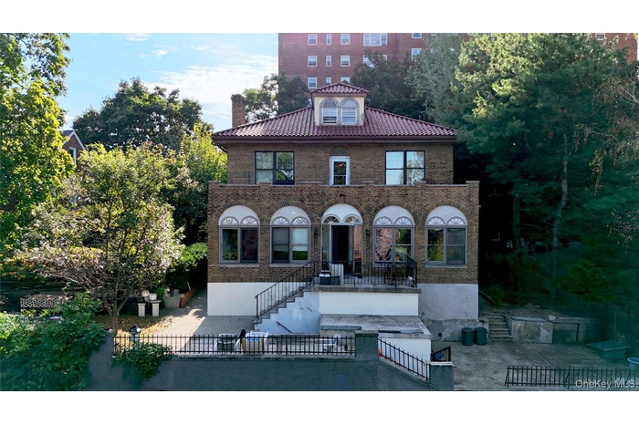 Back of property featuring brick siding, a chimney, a fenced front yard, a tiled roof, and a patio