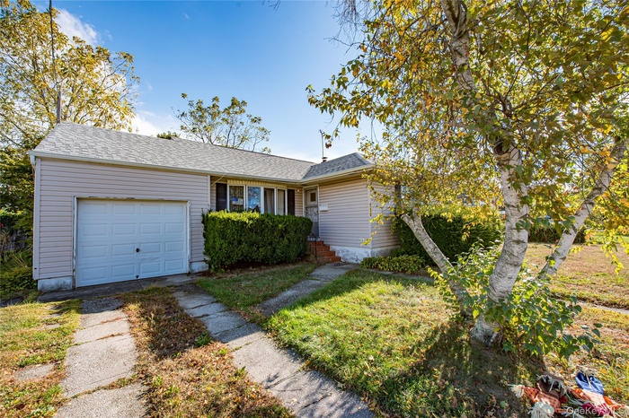 Ranch-style house featuring an attached garage, a shingled roof, and driveway