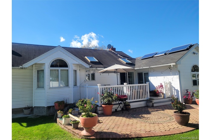 Back of house featuring a patio, roof mounted solar panels, a deck, a yard, and roof with shingles