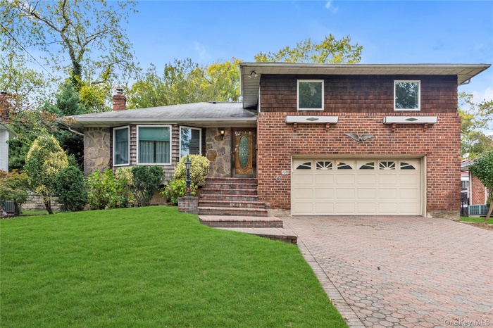 Tri-level home with decorative driveway, a front yard, a chimney, and a garage