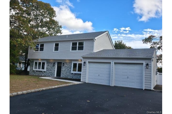 View of front facade with stone siding, driveway, an attached garage, and roof with shingles