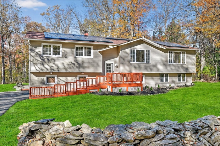 Back of property featuring roof mounted solar panels, a deck, and a lawn