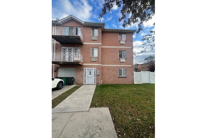 View of front facade with brick siding, a front yard, a balcony, and driveway
