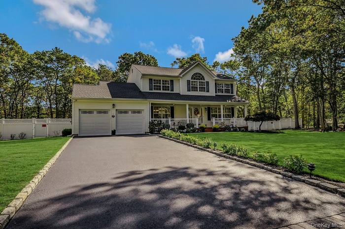 Colonial home featuring covered porch, asphalt driveway, a garage, and a shingled roof