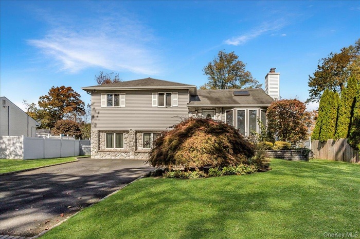 Split level home featuring driveway, stone siding, and a chimney