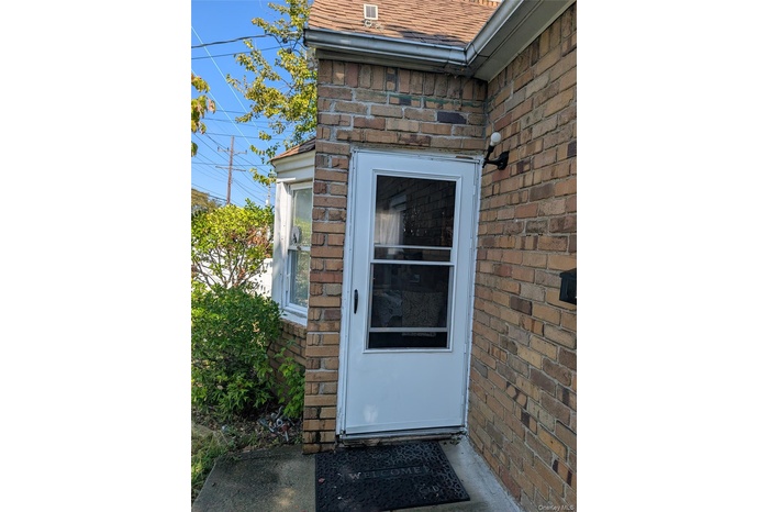 Doorway to property featuring brick siding and roof with shingles
