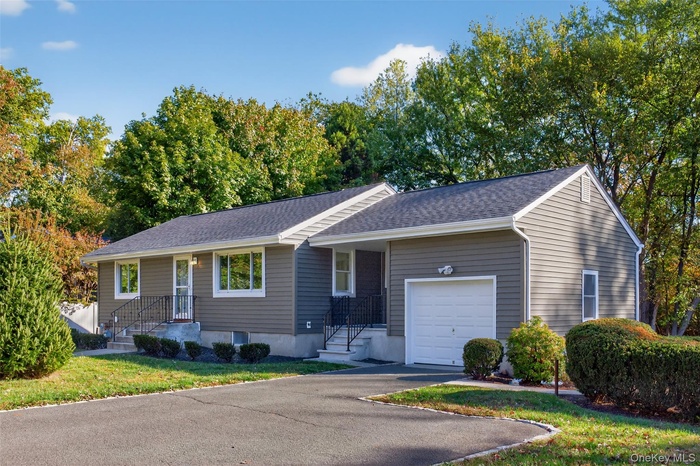 Ranch-style house featuring an attached garage, a shingled roof, asphalt driveway, and a front yard