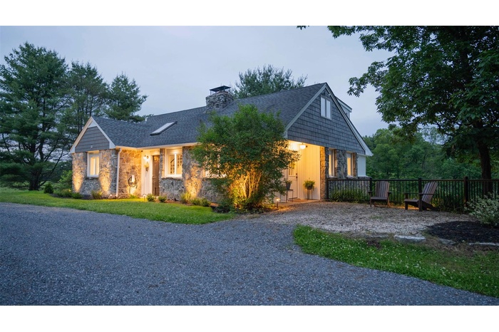 View of front of home featuring stone siding, a chimney, and a shingled roof