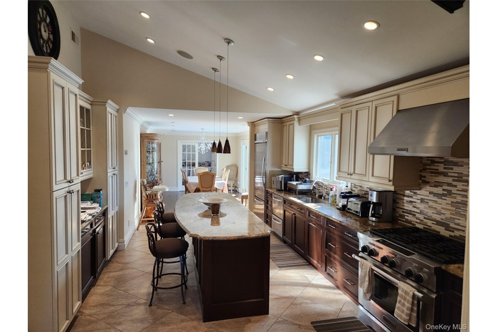 Kitchen featuring lofted ceiling, appliances with stainless steel finishes, recessed lighting, a kitchen breakfast bar, and cream cabinets