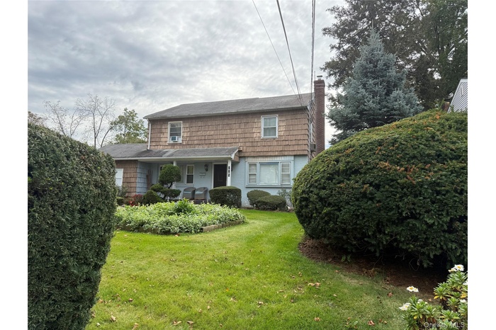 View of front facade with a chimney, a front yard, and covered porch