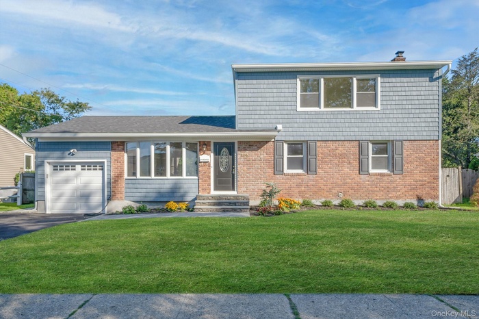 View of front of property featuring an attached garage, asphalt driveway, brick siding, and a chimney
