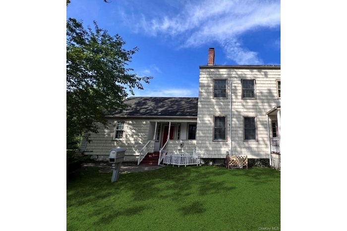 Back of house with a porch, a lawn, and a chimney