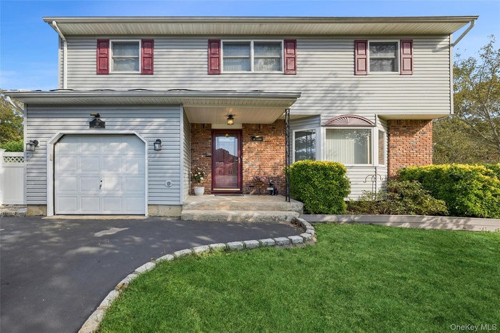 Traditional-style colonial house featuring a front yard, driveway, a garage, and brick siding