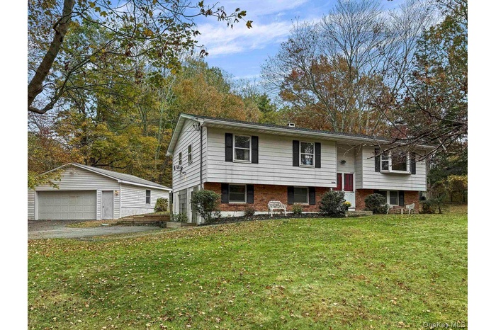 Raised ranch featuring brick siding, an outbuilding, a front lawn, and a garage