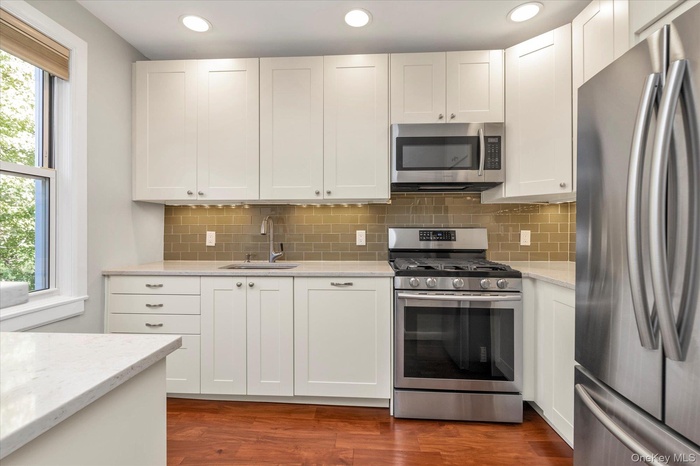 Kitchen featuring appliances with stainless steel finishes, light stone counters, white cabinetry, tasteful backsplash, and dark wood-style flooring
