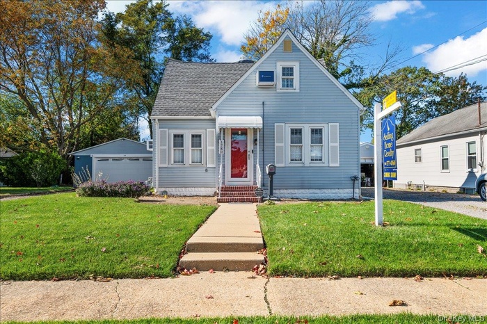 View of front of home with a front lawn, a shingled roof, a garage, and an outdoor structure