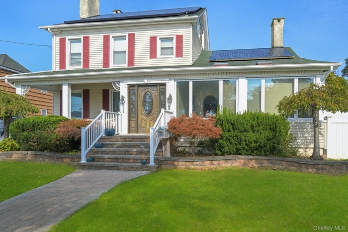 View of front of house with solar panels, a chimney, and a front lawn