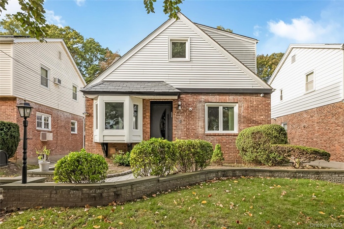 Bungalow with a front lawn, brick siding, and an AC wall unit