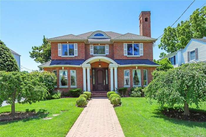 View of front of home featuring a chimney, brick siding, and a front lawn