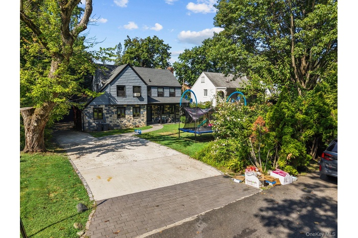 View of front of house featuring a trampoline, concrete driveway, stone siding, a chimney, and a front yard