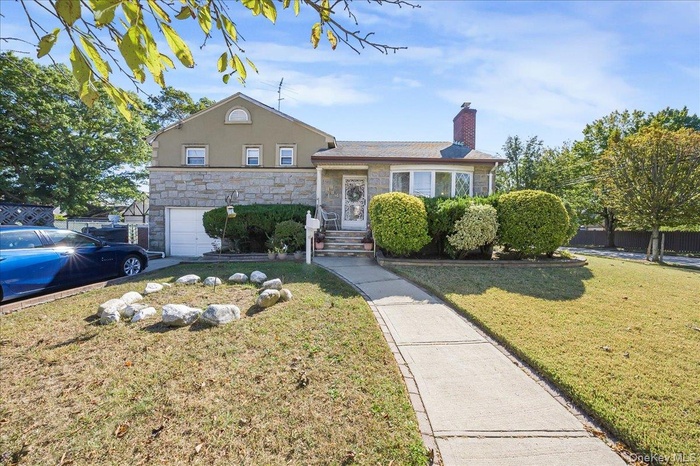 Split level home with stone siding, a front lawn, and a garage