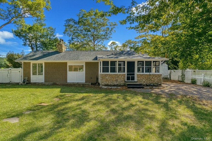 View of front of property with a chimney, stone siding, a sunroom, and a shingled roof