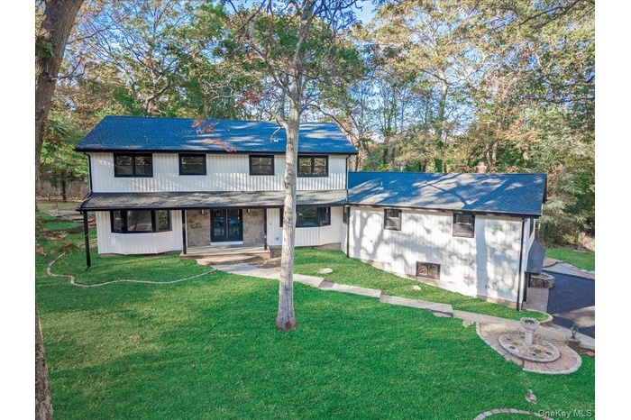 View of front facade featuring a front lawn, covered porch, roof with shingles, and view of scattered trees