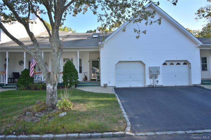 View of front of property with covered porch, driveway, a front yard, roof with shingles, and a garage