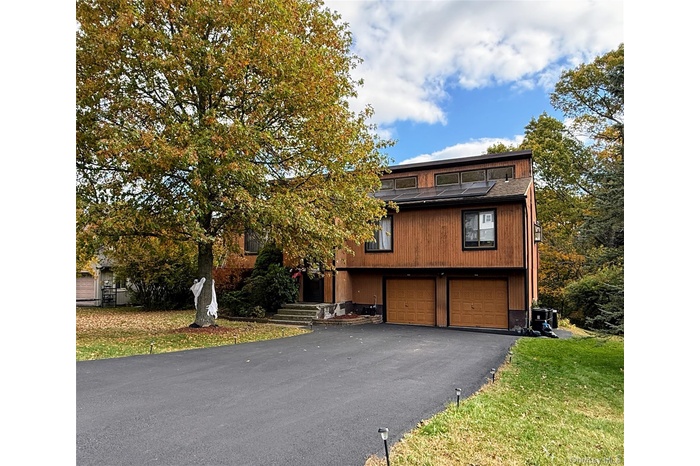 View of front of house featuring driveway, an attached garage, a front yard, and roof mounted solar panels