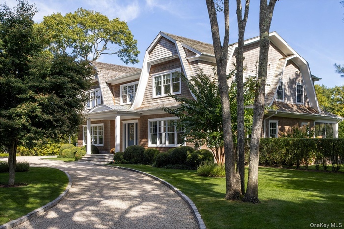 Shingle-style home with a gambrel roof, a front lawn, covered porch, and driveway