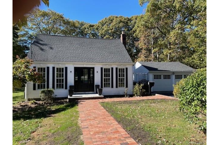View of front of property featuring an outbuilding, a chimney, a front yard, and roof with shingles