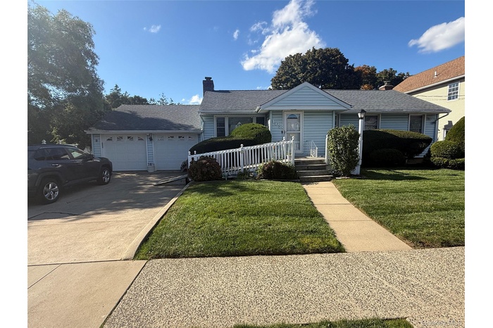 View of front of property featuring concrete driveway, a front yard, a chimney, and a garage