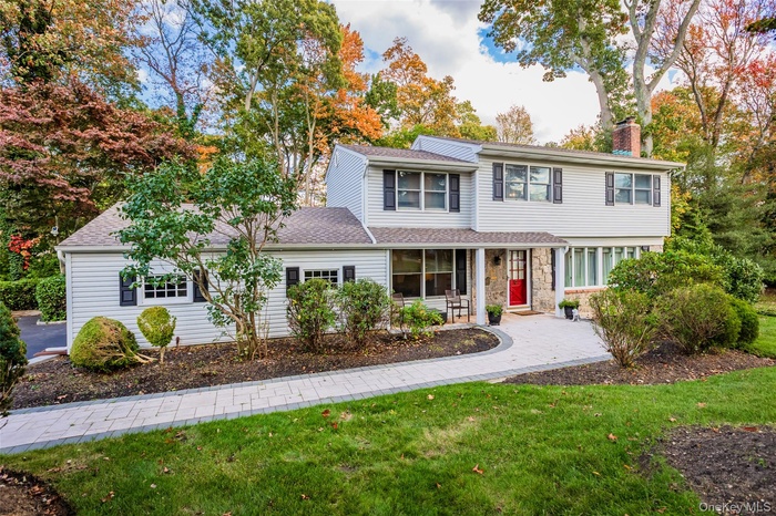Traditional-style home featuring a front yard, a chimney, roof with shingles, and stone siding