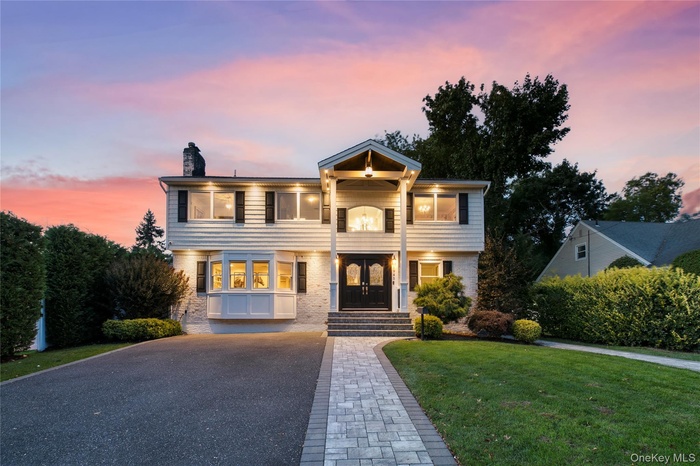 View of front of home featuring brick siding, asphalt driveway, a chimney, and a front yard